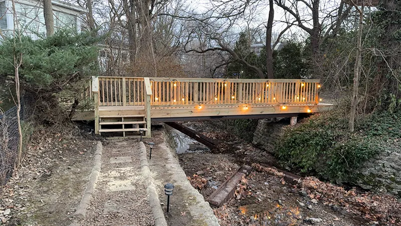 Elevated wooden deck with string lights, overlooking a sloped backyard and trees.