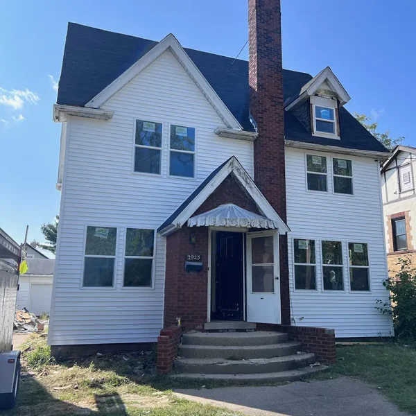 Two-story house with white siding, a brick chimney, and a covered front porch.