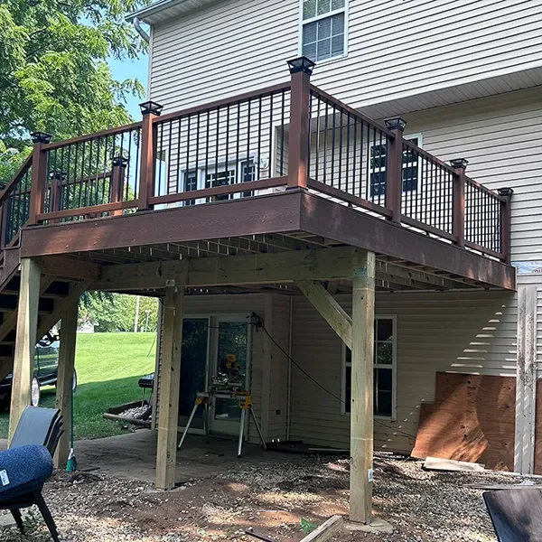 Elevated backyard deck with brown railings and stairs, providing access to a sliding glass door.