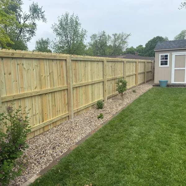 A long, newly installed wooden privacy fence with vertical pickets runs along the edge of a well-maintained backyard.